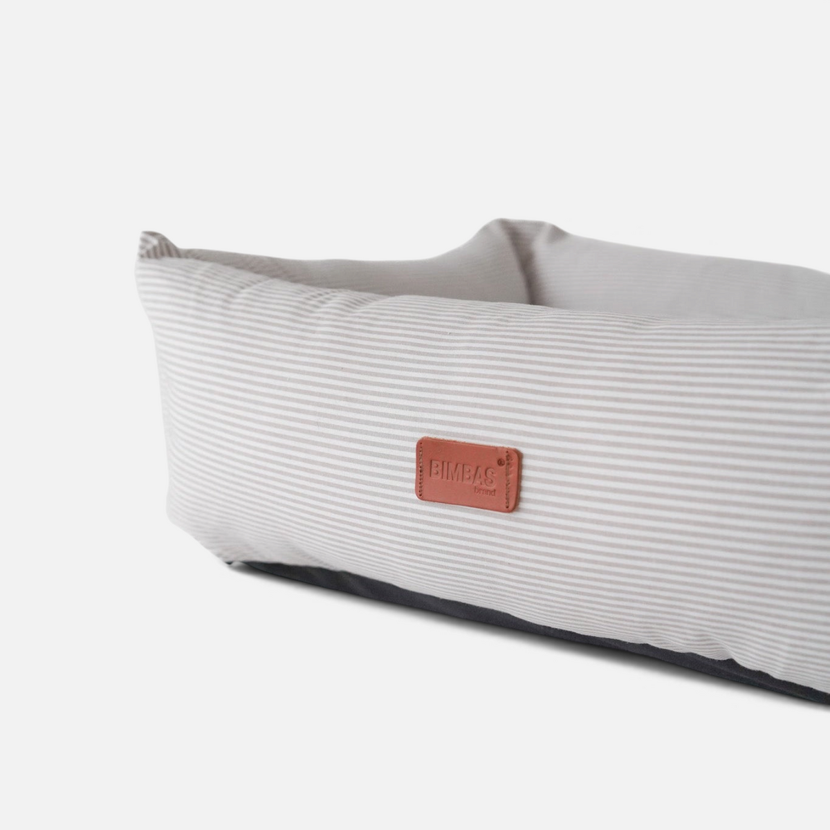 Cama para perros BIMBAS BRAND desenfundable con tejido de rayas beige y etiqueta de cuero sobre fondo blanco